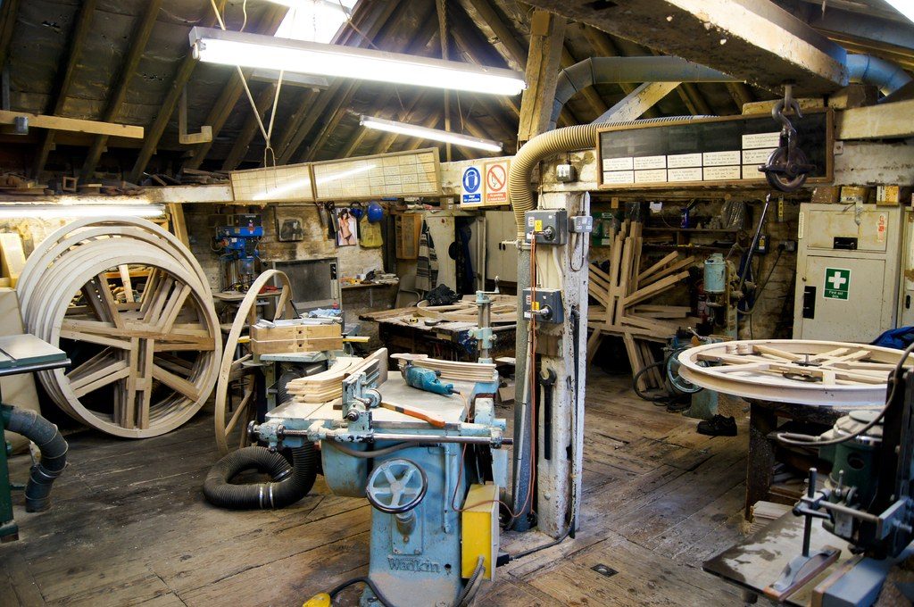 Busy traditional workshop with workbenches and large wooden wheels